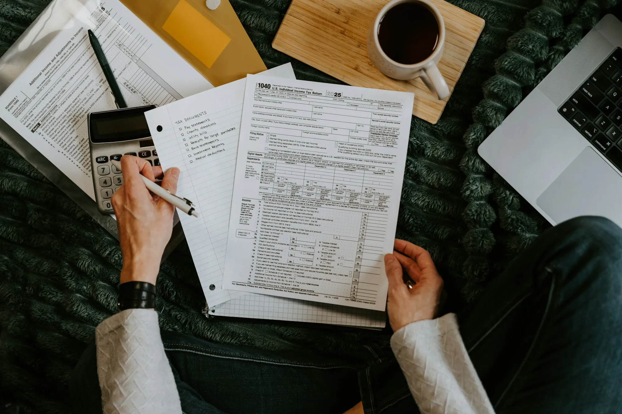 Hands going through printed invoices next to a calculator and a laptop