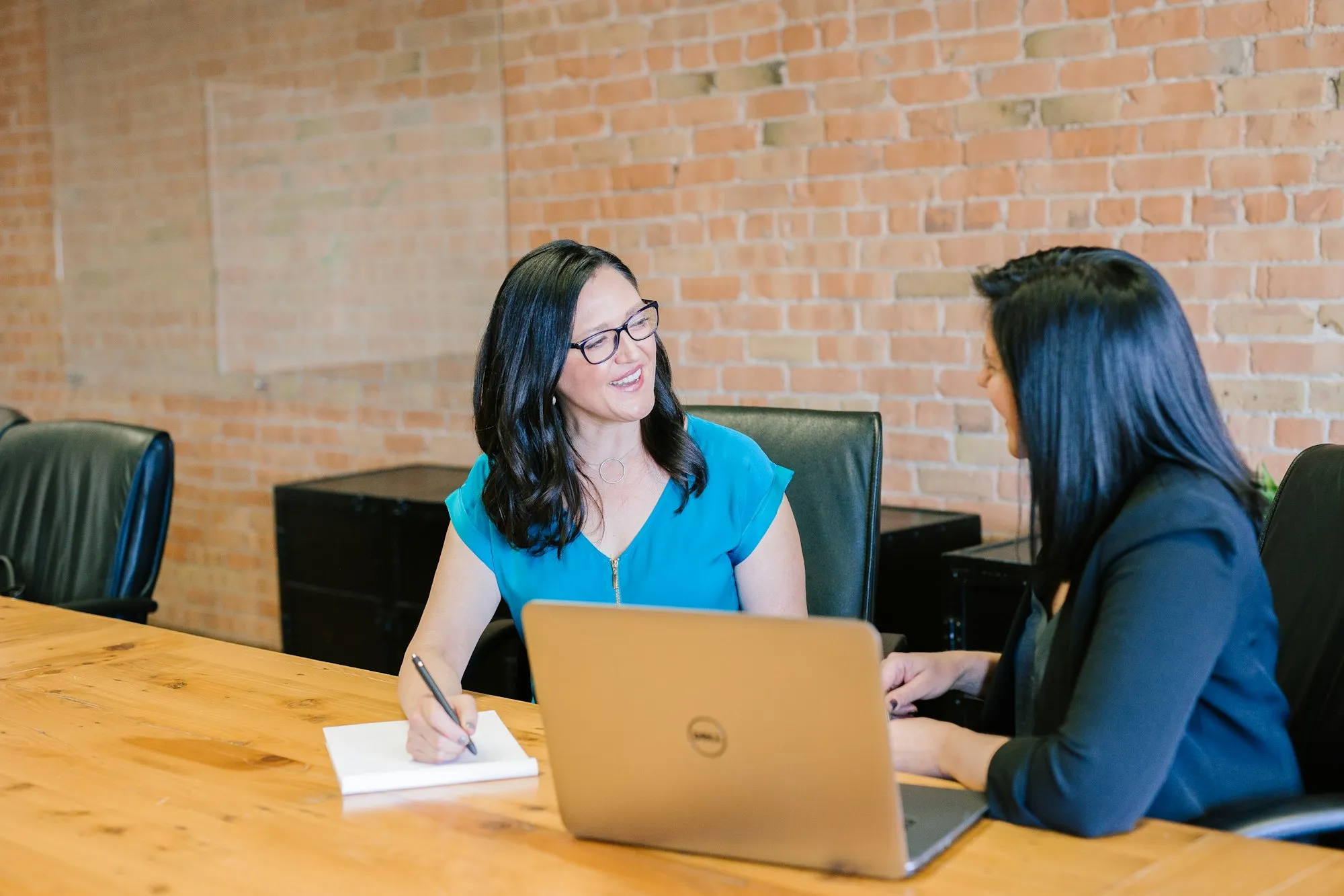 An HR manager taking notes during a one-to-one with an employee at a wooden table