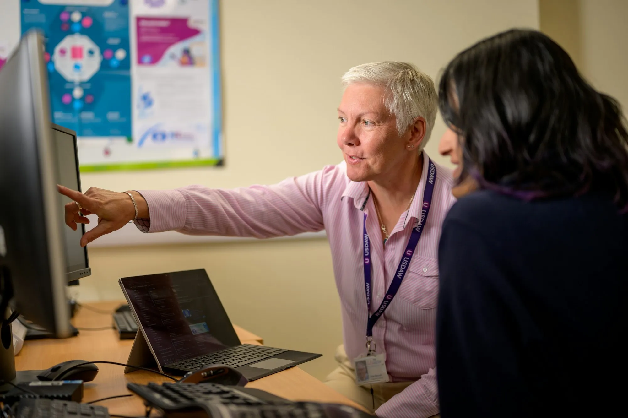 An IT technician pointing at a screen to walk a colleague through a fix at her desk