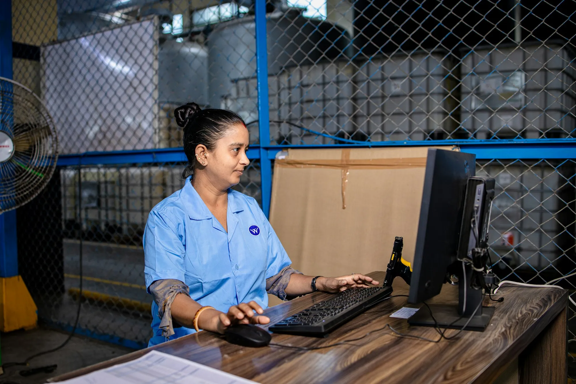 A warehouse employee working at a computer next to the stock shelves