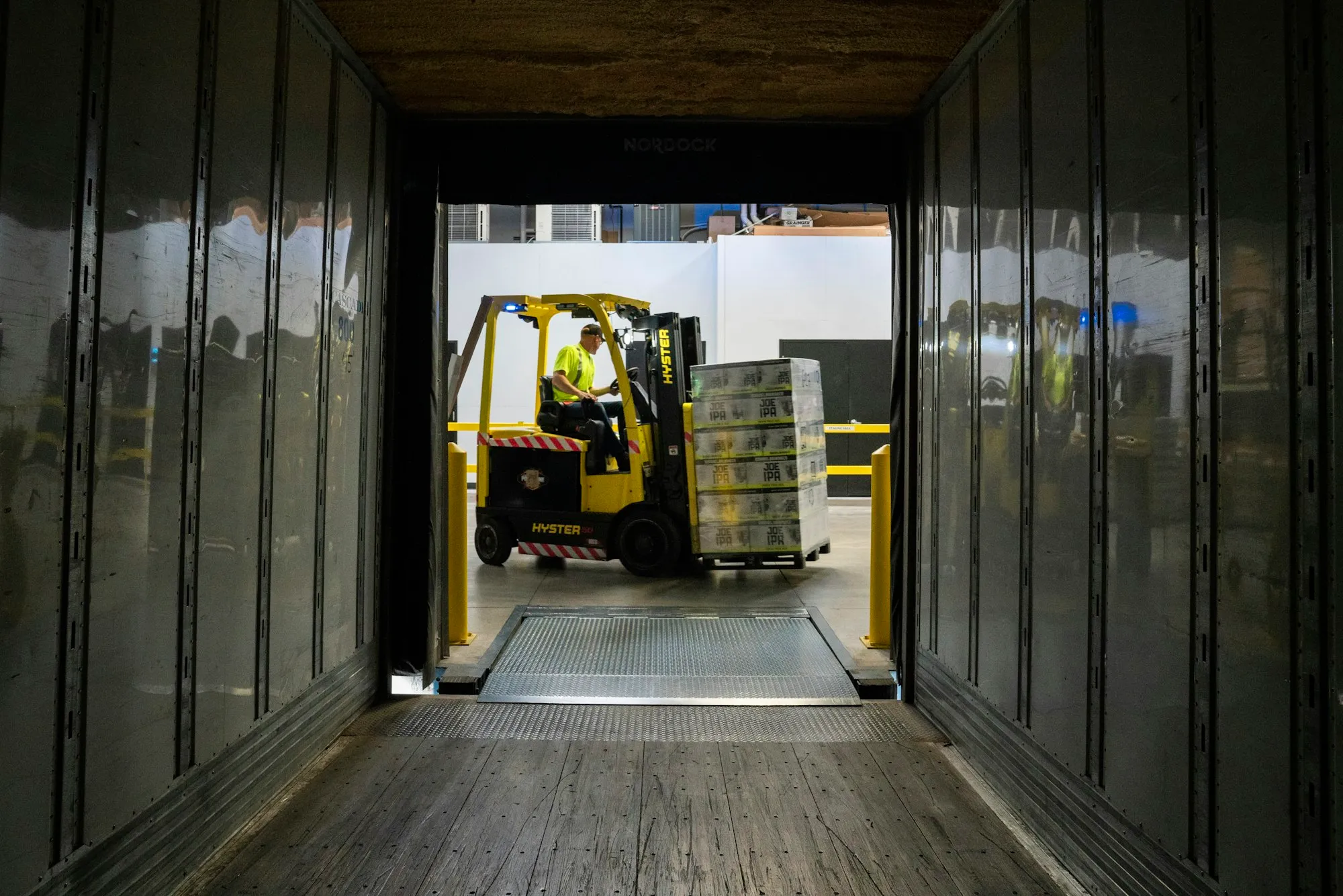 A forklift driver loading a pallet into a trailer, seen from inside the truck