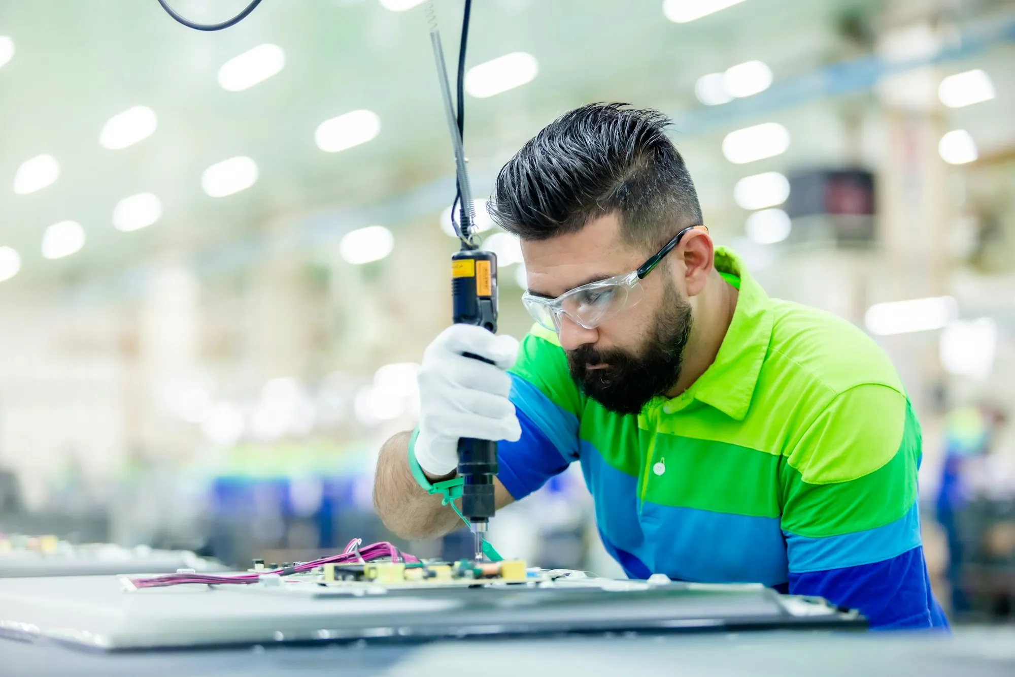 Un technicien en lunettes de protection assemble une carte électronique sur une ligne de production