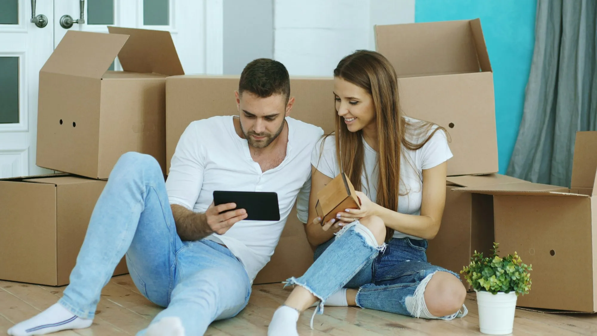 Un couple assis parmi les cartons consulte une tablette dans son nouveau logement