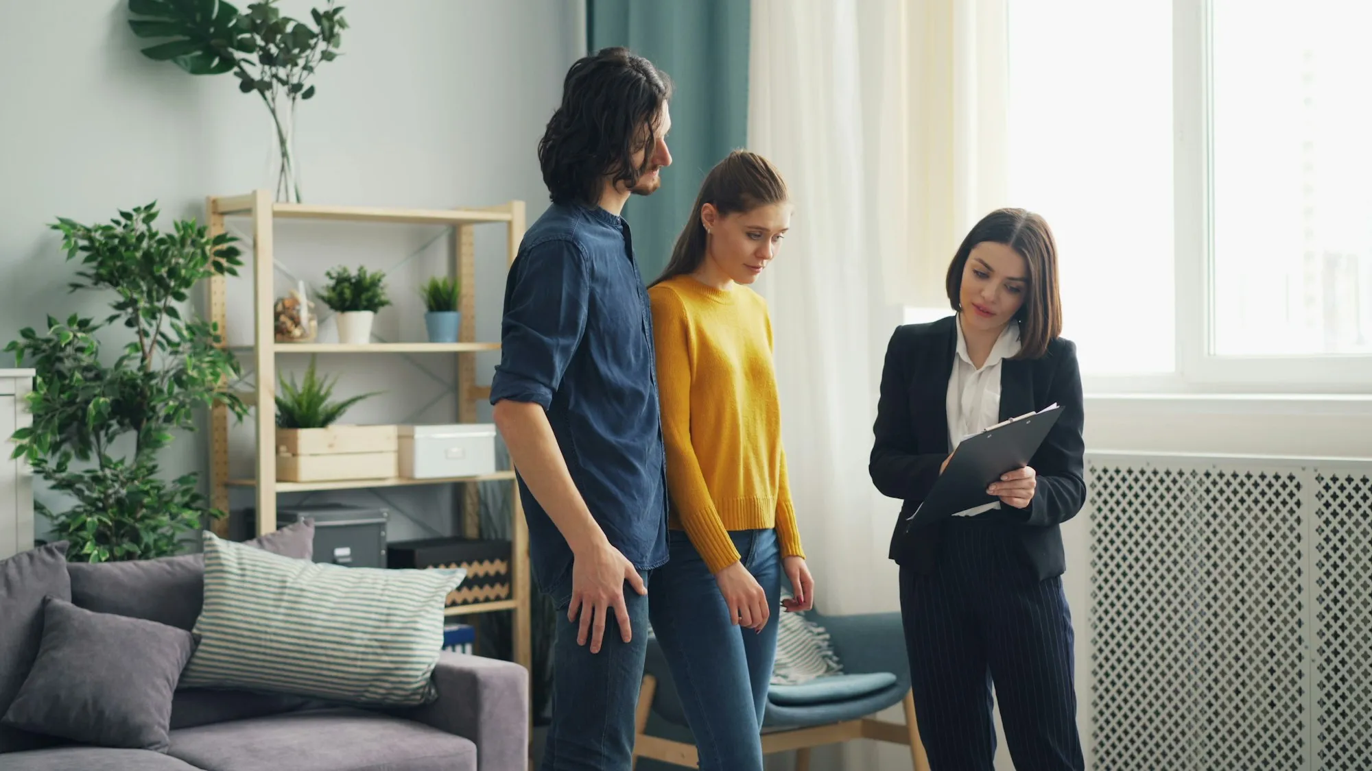 An agent with a tablet showing a living room to a couple
